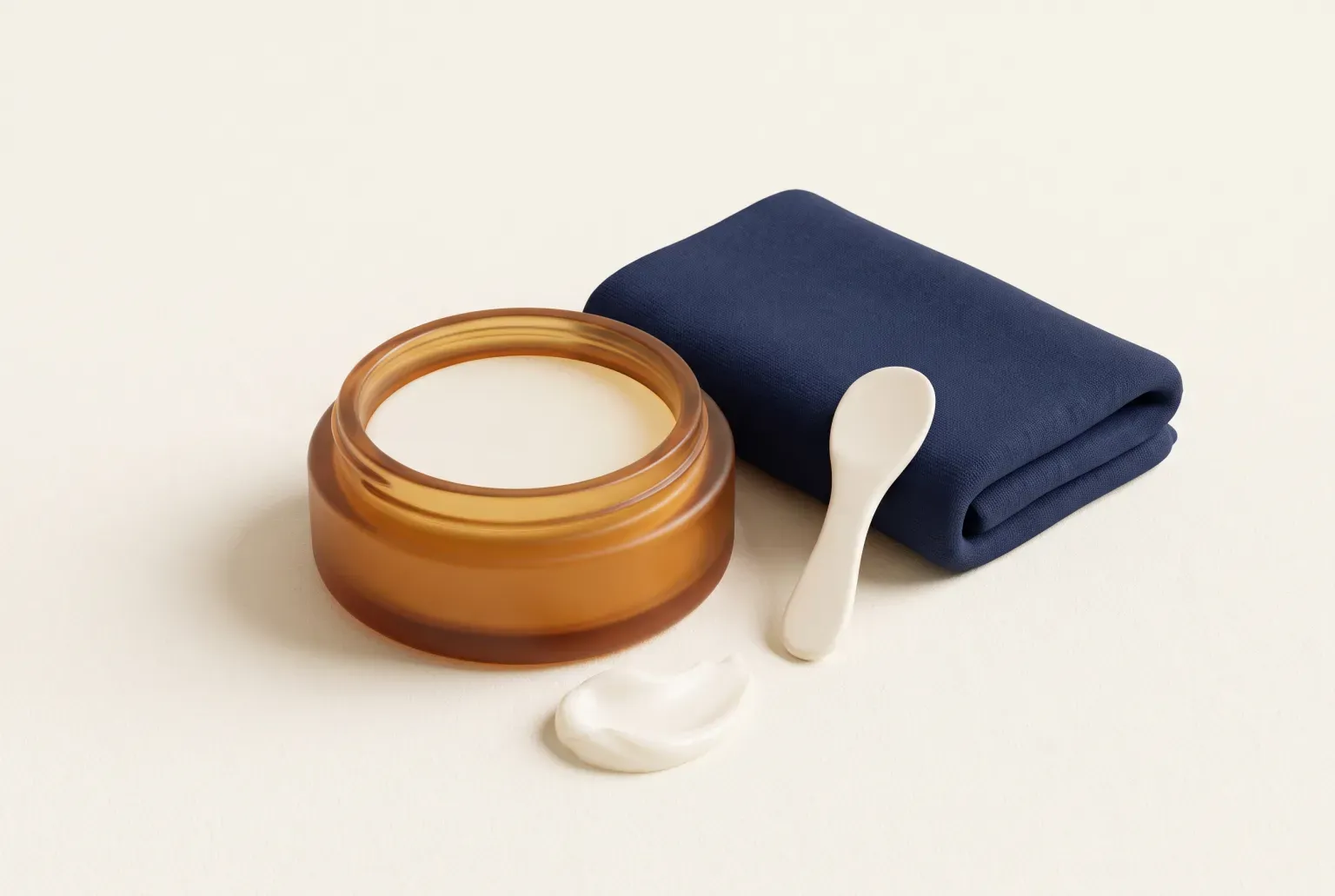 Illustration: a shallow amber glass jar of pale balm with a small cream spatula, a swirl of balm and a folded navy washcloth on a cream surface, drawn as a soft 3D render. Not a real product.