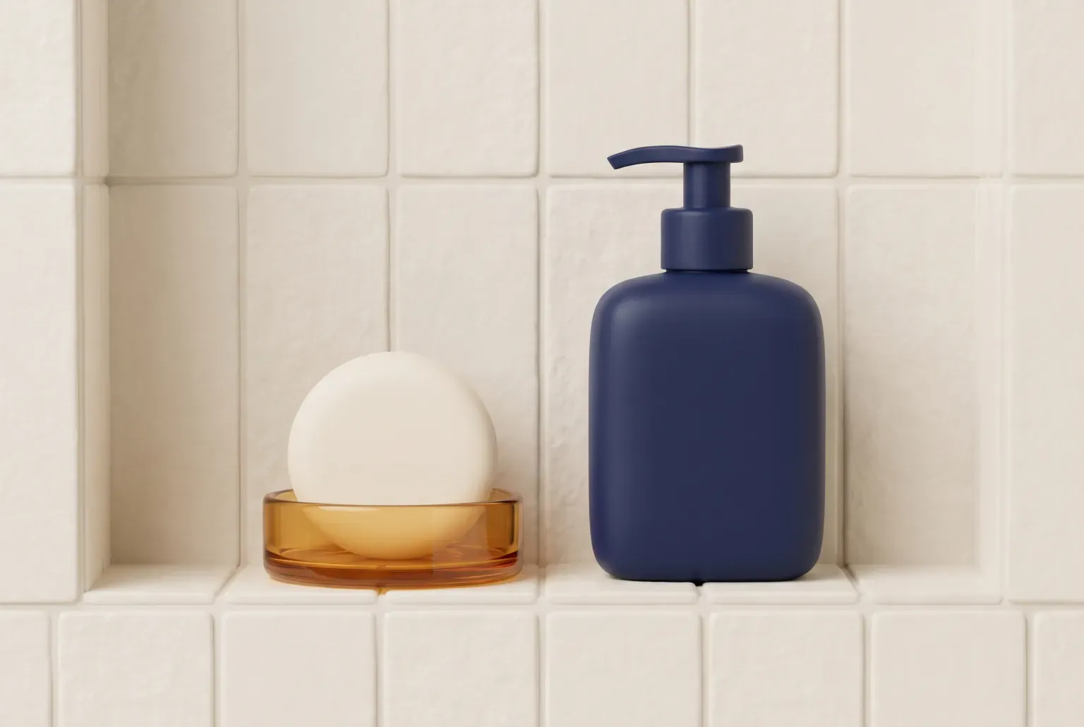 Illustration: a round cream bar of soap in an amber glass dish beside a navy pump bottle with a blank surface on a cream tiled shower shelf, drawn as a soft 3D render. Not a real product.