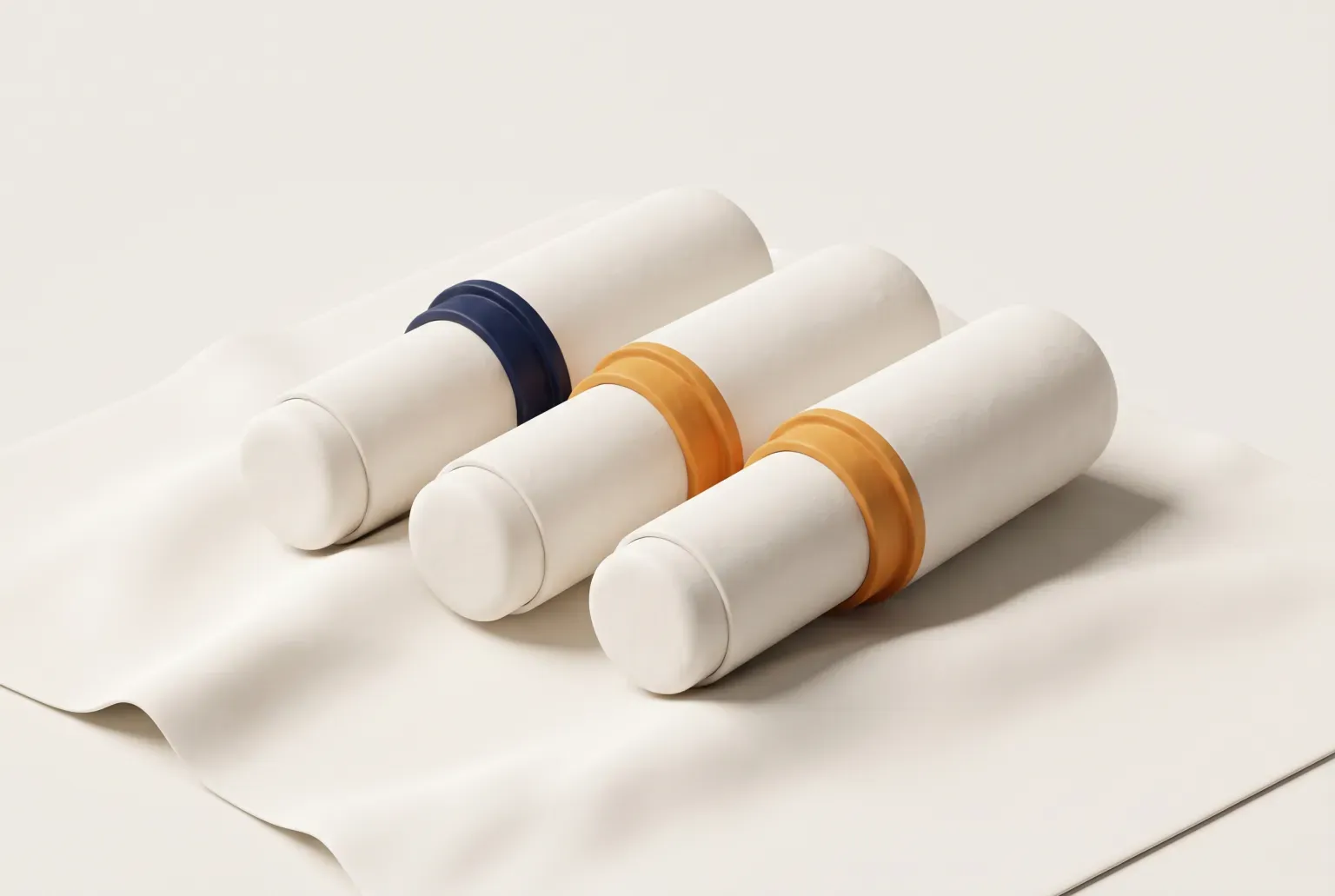Illustration: three plain cream makeup sticks with cream caps and colored bands lying side by side on a softly folded cloth, drawn as a soft 3D render. Not a real product.