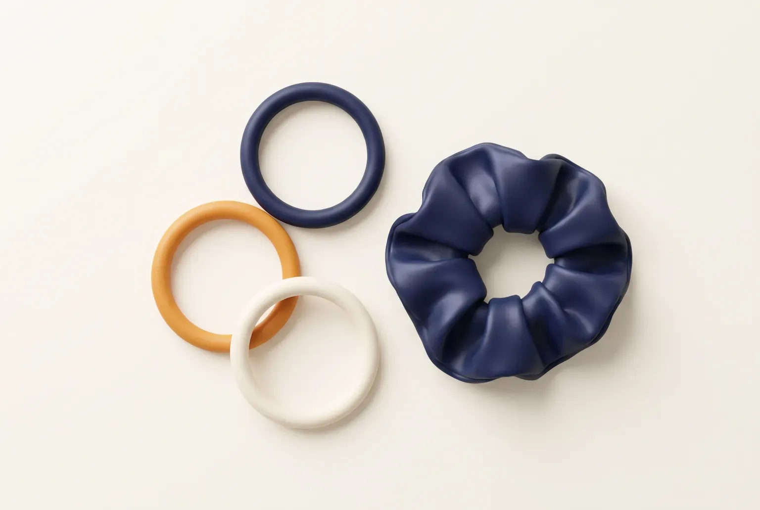 Illustration: three plain round hair ties in navy, amber and cream beside a navy satin scrunchie on a smooth cream surface, drawn as a soft 3D render. Not a real product.