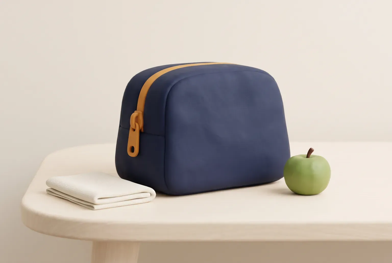 Illustration: a rounded navy soft lunch bag with an amber zipper on a pale wooden desk beside a folded cream napkin and a green apple, drawn as a soft 3D render. Not a real product.