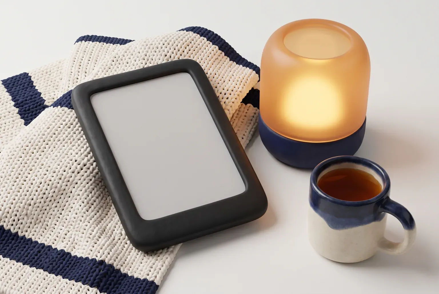 Illustration: a plain black e-reader with a blank screen on a knitted blanket beside a glowing lamp and a mug of tea, drawn as a soft 3D render. Not a real product.