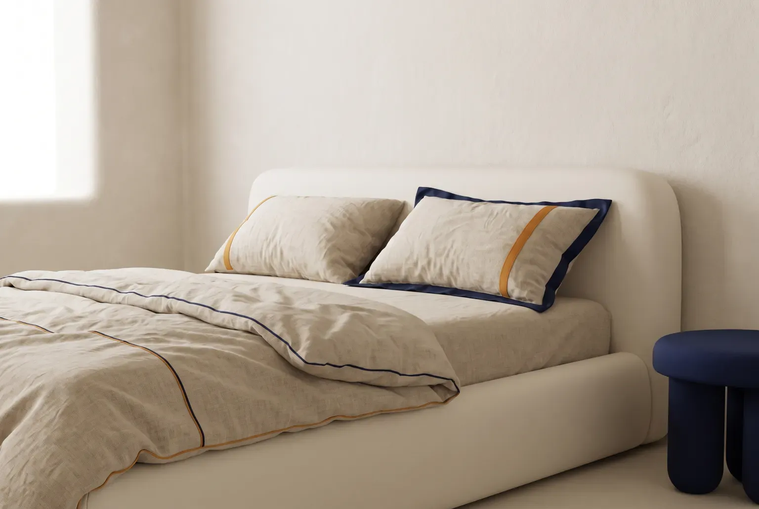 Illustration: a low cream bed made up with rumpled natural linen sheets and two pillows, a navy stool beside it, drawn as a soft 3D render. Not a real product.
