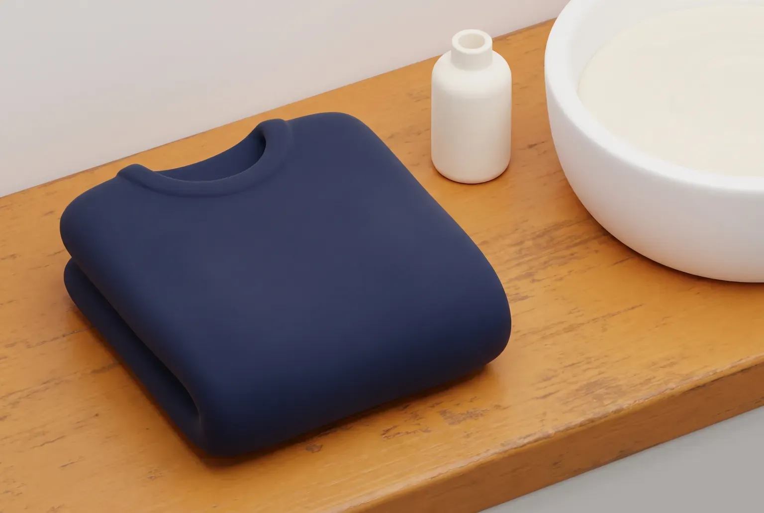 Illustration: a folded navy sweater on a wooden counter beside a small cream bottle and a white basin of water, drawn as a soft 3D render. Not a real product.
