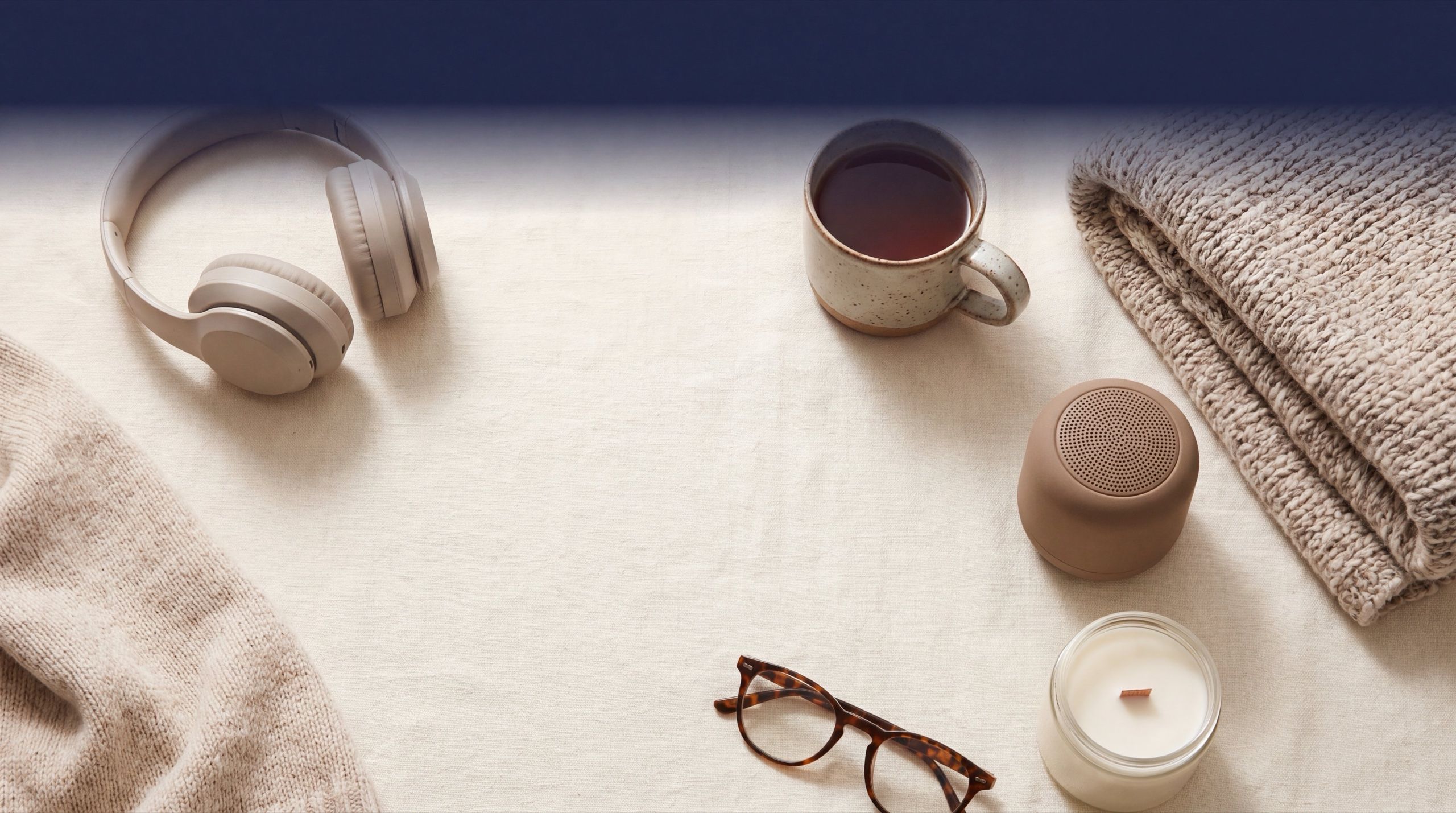 Headphones, a mug of tea, a speaker, a candle and glasses on a linen table